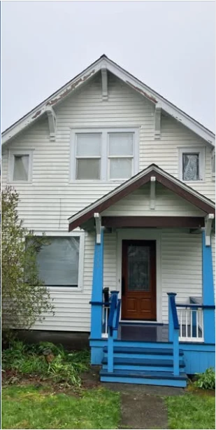Before painting: a light-colored house with white upper trim and blue porch steps